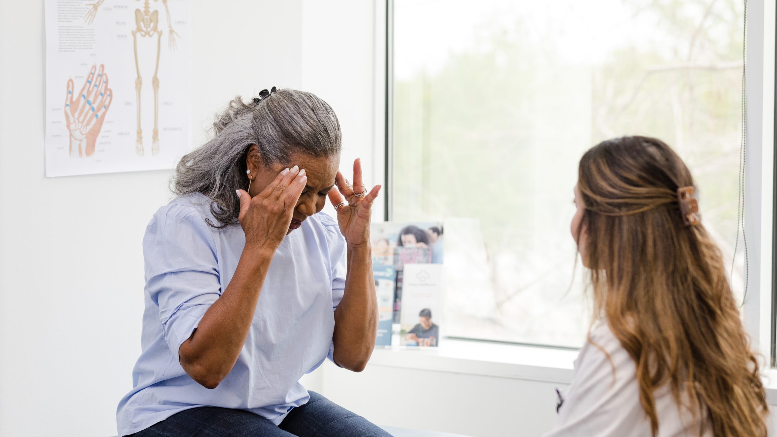 Older woman holding her head in pain while talking with a female healthcare specialist.