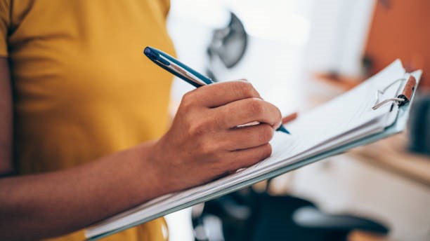Woman writing on a clipboard with a pen.