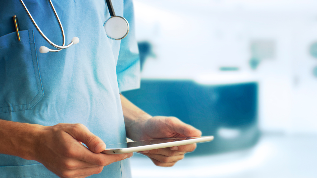 Male physician wearing a stethoscope holds an iPad in his hands.
