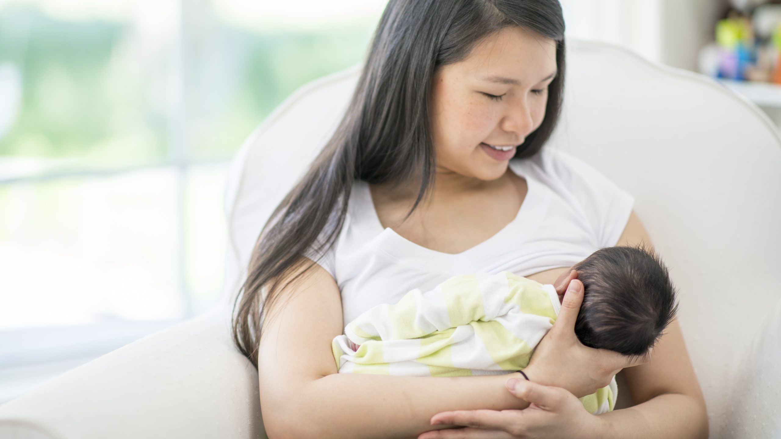 A woman breastfeeds her baby while seated.