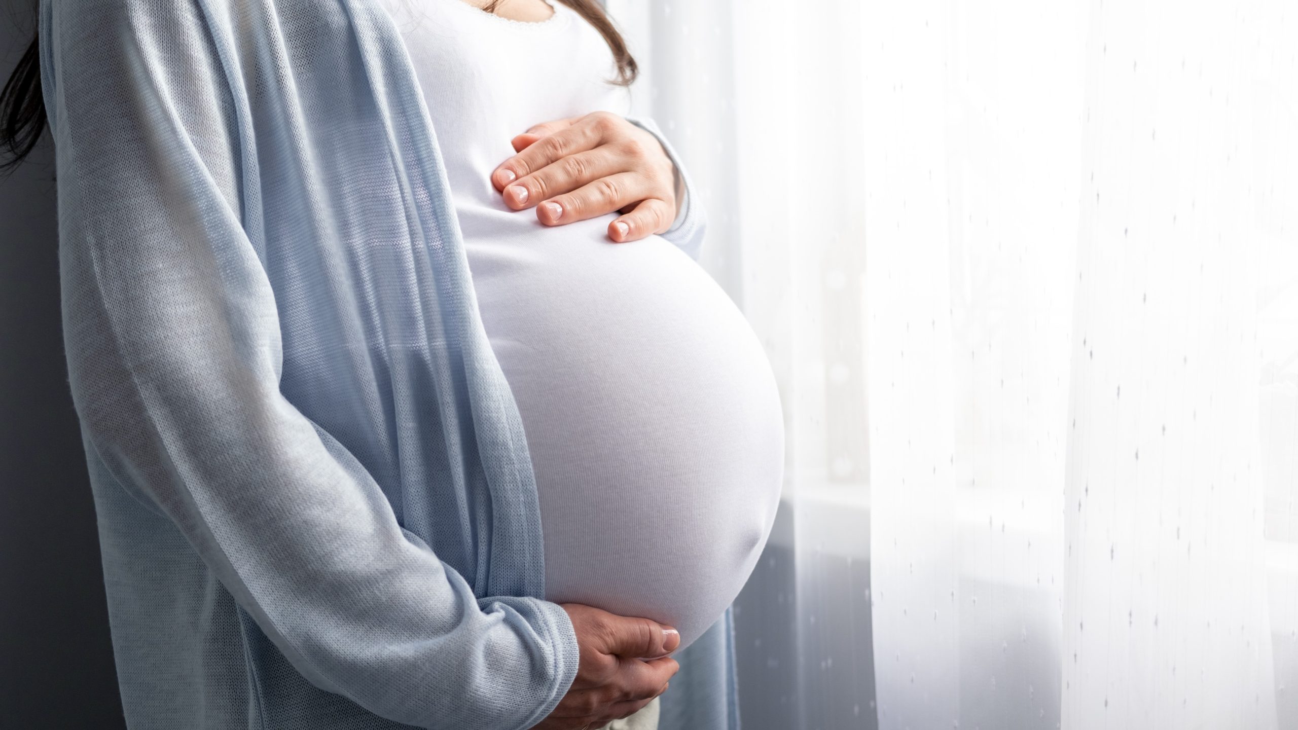 A pregnant woman with hands on her abdomen.