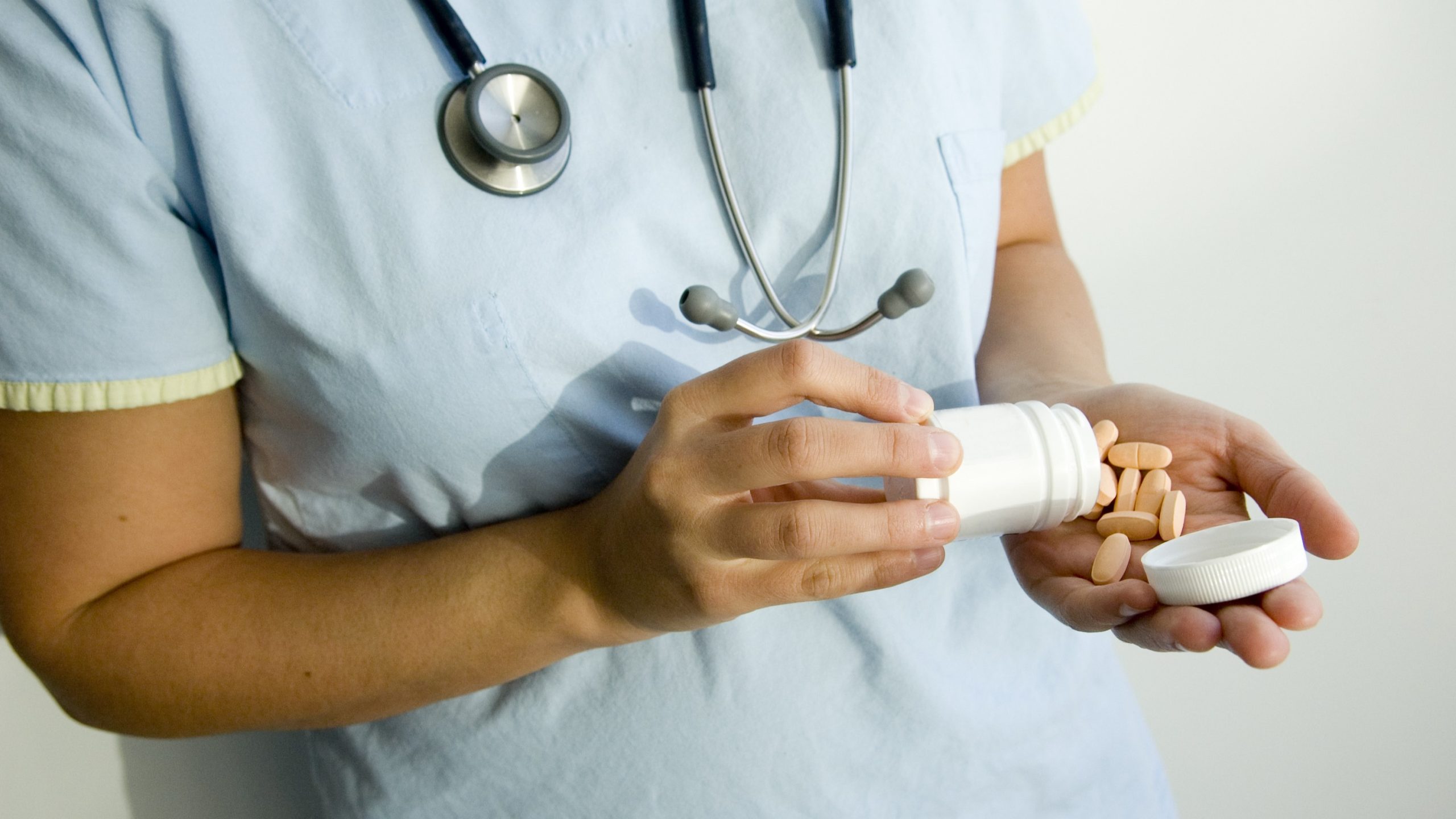 Female doctor pouring pills from a bottle into her hand.