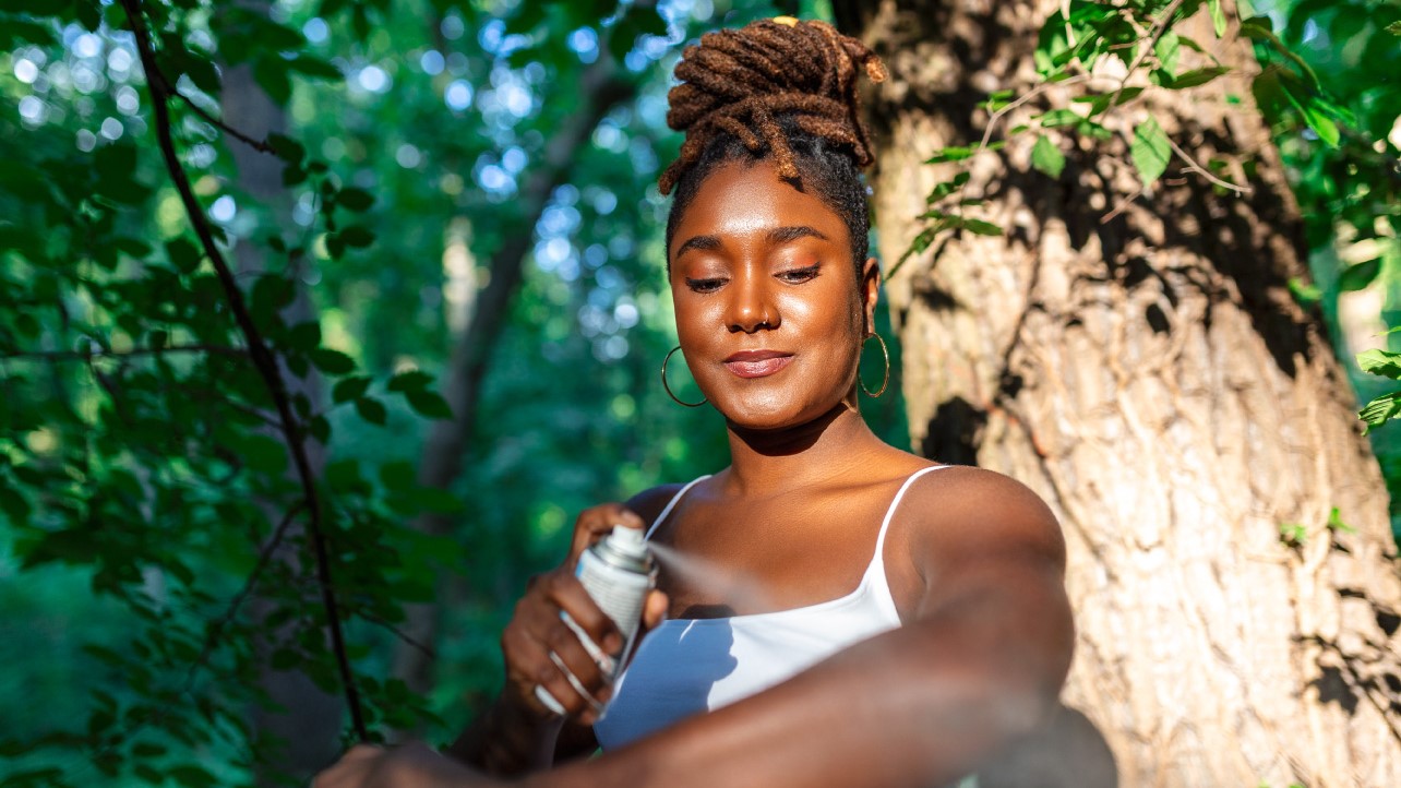 Woman outdoors in a forest spraying insect repellent on her arm.