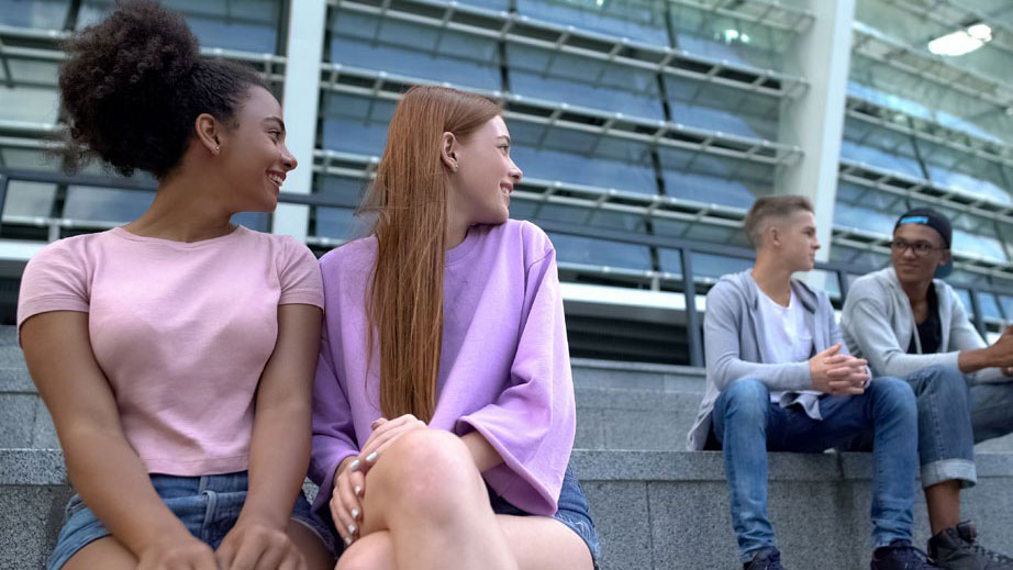 Two female teenagers sitting next to each other and looking over their shoulders at two male teenagers.